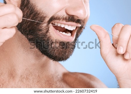 Dental, floss and oral hygiene with a man in studio on a blue background cleaning his teeth for healthy gums. Dentist, healthcare and mouth with a young male flossing to remove plague or gingivitis Royalty-Free Stock Photo #2260732419