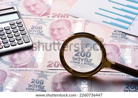 Financial concepts, close up two hundered turkish currency with magnifying glass, calculator and business graphs Royalty-Free Stock Photo #2260736447