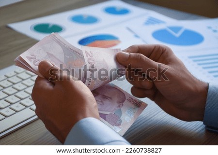Financial concepts, businessman counting turkish money, two hundered lira on the office desk with business graphs