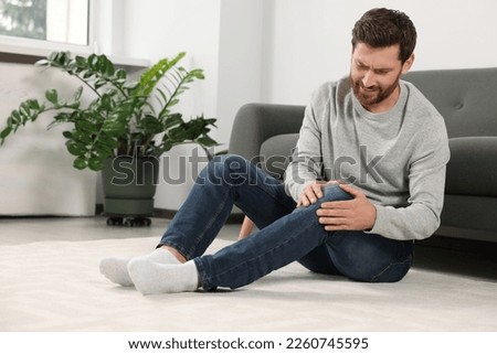 Man suffering from leg pain near sofa in room Royalty-Free Stock Photo #2260745595