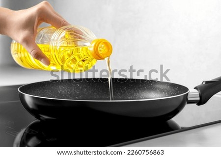 Woman pouring cooking oil from bottle into frying pan on stove, closeup Royalty-Free Stock Photo #2260756863