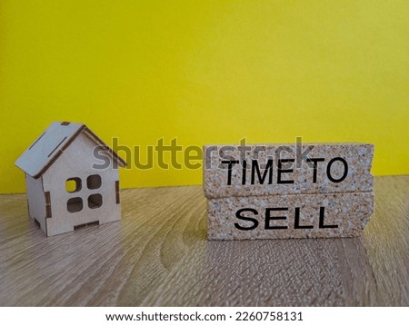 Time to sell house symbol. Concept words 'Time to sell' on wooden blocks near miniature houses. Beautiful yellow background, copy space. Business and time to sell house concept.