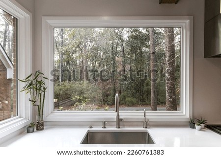 A large farmhouse single farm house sink with a massive picture window with a view of the wooded lot yard.