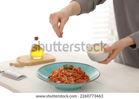 Food stylist adding grated cheese to spaghetti at white wooden table in photo studio, closeup