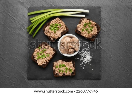 Tasty sandwiches with cod liver, salt and green onion on grey table, top view