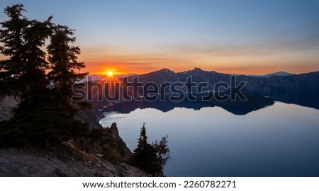 Orange Rays from Sunset Behind Mountains Over Crater Lake National Park Royalty-Free Stock Photo #2260782271