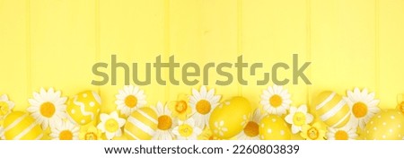 Yellow Easter eggs and white daisy flowers. Top down view bottom border against a vibrant yellow wood banner background. Copy space.