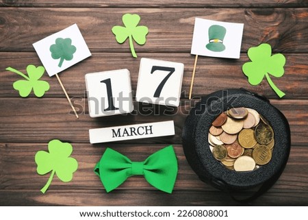Pot of coins, cube calendar, clover leafs, bow tie and flags with pictures on brown wooden background. Concept St.Patrick's Day