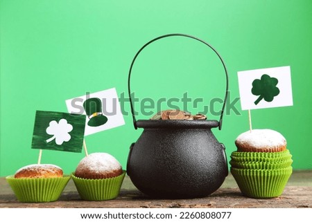Pot of coins and cupcakes with pictures of hat and clover leafs on green background