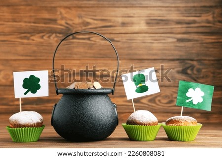 Pot of coins and cupcakes with flags and pictures of hat and clovers on brown wooden background