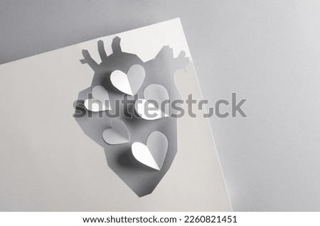 Paper-cut hole in the shape of an anatomical heart and a lot of hearts on a gray background. Creative idea, love concept