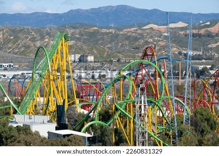 Wide view of colorful roller coaster rides at an amusement park, sunny day mountains in background. Six Flags Magic Mountain Six Flags Hurricane Harbor Royalty-Free Stock Photo #2260831329