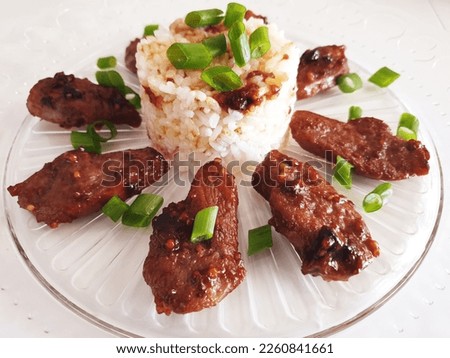 Rice with duck sprinkled with green onions on a round transparent glass plate on a white background. Restaurant serving food. Asian duck with rice.