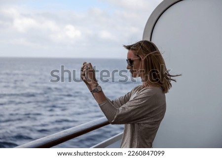 A woman taking pictures of Cape Horn from a cruise ship balcony