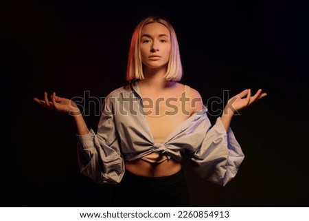 Content fair haired woman in stylish clothes looking at camera against black background