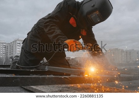A welder in a suit and mask welds metal against the sky, welding work, a lot of sparks Royalty-Free Stock Photo #2260881135