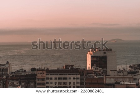 Low-key photo of the ocean as it blends with the pink sky in this sunset shot. The degraded buildings in the foreground contrast with the serene sea, while boats drift peacefully in the distance