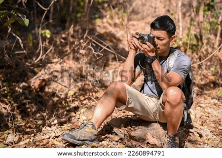 Handsome and active Asian man in active outfit taking a picture with film camera while hiking at the mountain trail. outdoor activity and sport concept