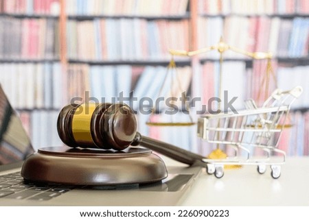 Consumer rights and protection, e-commerce law concept : Wooden judge's gavel rests on a laptop computer with a shopping cart and a balance scale of justice behind, symbols of fairness and commerce. Royalty-Free Stock Photo #2260900223