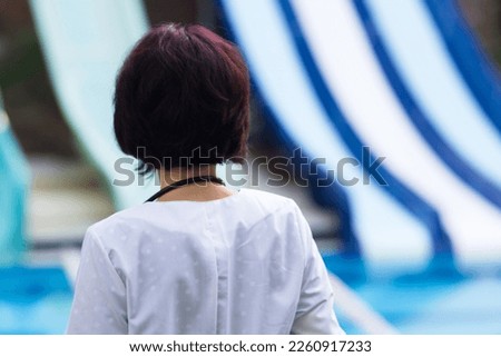 nurse in white coat stands with her back turned and watches people bathing in the water park.,