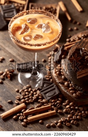 Irish coffee and cream cocktail in a glass with ice. Coffee beans, cinnamon, anise, and pieces of chocolate are scattered on the table. 