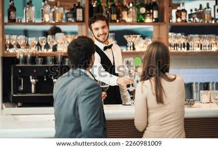 Bar, barman and serve a couple alcohol drinks on a date with hospitality, happy and smile at a hotel. Waiter, bartender and server help customers or people with good service for a celebration Royalty-Free Stock Photo #2260981009