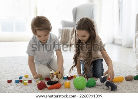 Two cute engaged little brother and sister kids playing with toys on soft white carpet on floor, enjoying leisure, playtime, developing game with fabric animals and plastic building blocks Royalty-Free Stock Photo #2260991099