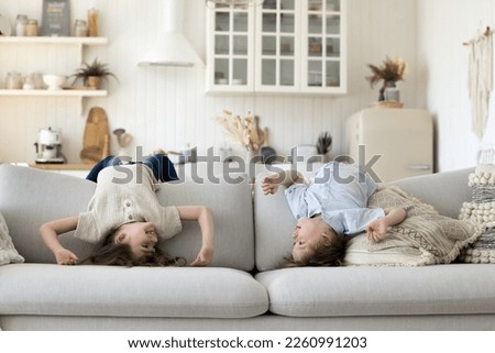 Two cute energetic sibling kids having fun at home, enjoying activity, stretching on sofa, hanging on back upside down, playing active games, talking, smiling, laughing Royalty-Free Stock Photo #2260991203