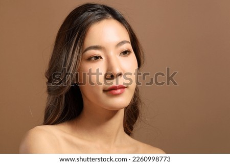 The beautiful  Asian woman showing skin with brown background holding monstera leaf.