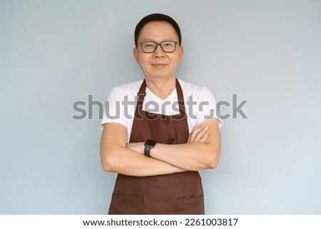 Happy middle aged Asian man waiter Entrepreneur looking at camera. Chinese millennial businessman wear apron arms crossed isolated green pastel color background. Start up small business owner concept.