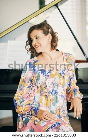 Portrait of beautiful young woman sitting next to piano, wearing colorful dress 