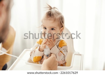 Portrait of a little girl inhaling medicine on nebulizer and holding it on her own. Royalty-Free Stock Photo #2261017629