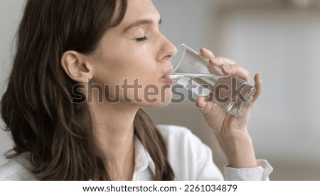Pleased thirsty young woman drinking clear natural water from glass with closed eyes, recovering healthy hydration balance, keeping diet, refreshing. Banner shot, side view Royalty-Free Stock Photo #2261034879