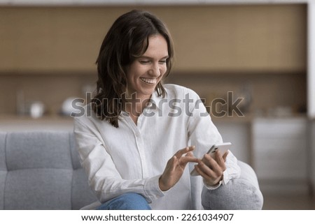Joyful young cellphone user woman typing on gadget, chatting online, making video call, using online app on smartphone for Internet communication, smiling, laughing, looking at screen Royalty-Free Stock Photo #2261034907