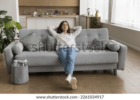 Relaxed sleepy young woman sitting on sofa, leaning on back, stretching body, resting on comfortable couch, breathing fresh air, sleeping on break, enjoying calm silent leisure time Royalty-Free Stock Photo #2261034917