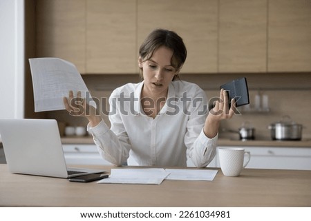 Stressed annoyed young laptop user woman reviewing domestic paper documents, using calculator, laptop, feeling frustrated, finding overspendings, financial mistakes Royalty-Free Stock Photo #2261034981
