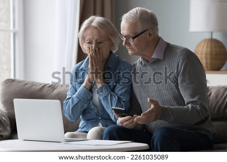 Shocked upset elderly couple getting bad news, finding fraud, money stealing, loss, overspending, financial problem, holding calculator, using laptop, staring at monitor Royalty-Free Stock Photo #2261035089