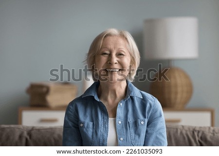 Happy cheerful elderly lady looking at camera with toothy smile, laughing, sitting on couch head shot portrait. Pretty senior woman talking on video call, enjoying conversation. Screen picture