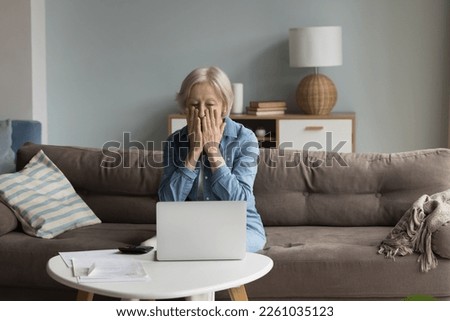 Shocked concerned senior accountant woman finding financial failure, mistake, bankruptcy, sitting at laptop, calculator, paper bills, covering face in panic attack, staring at screen Royalty-Free Stock Photo #2261035123