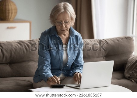 Serious mature retired pensioner woman calculating budget at home, counting investment income, making monthly payment on Internet, doing paperwork, economy, accounting job Royalty-Free Stock Photo #2261035137