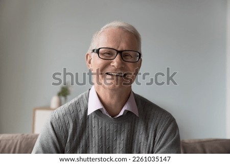 Happy positive old retired man in glasses sitting on couch at home, looking at camera, smiling, laughing. Male head shot portrait. Pensioner speaking on video call conversation. Screen photo Royalty-Free Stock Photo #2261035147