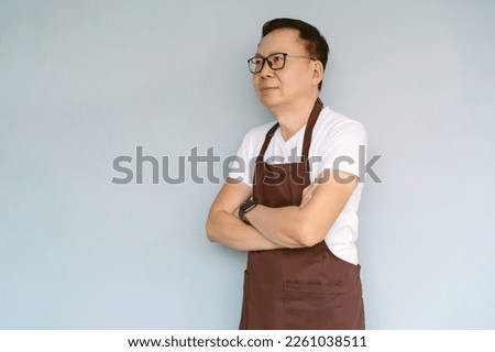Side view of middle aged Asian businessman wear apron folded arms and looking in distance thinking of future career opportunities and smiling standing against green pastel wall with copy space.