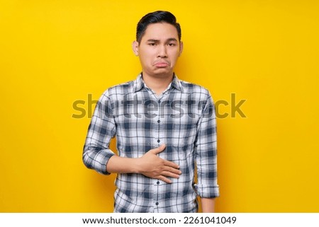 Young handsome Asian man wearing casual clothes keeps his hands on his stomach feeling hungry and wanting to eat delicious isolated on yellow background. People lifestyle concept Royalty-Free Stock Photo #2261041049