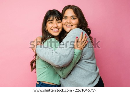 Gorgeous hispanic women best friends hugging sharing love looking at the camera on a pink background Royalty-Free Stock Photo #2261045739