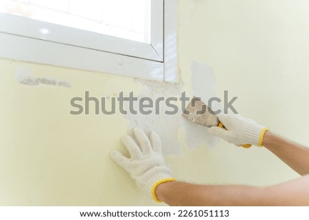 Hand painter man using scraper or spatula to remove old paint wall for cleaning, repair, preparing concrete wall before painting wall at home. Scraping to remove paint plaster peel. Painting concept. Royalty-Free Stock Photo #2261051113