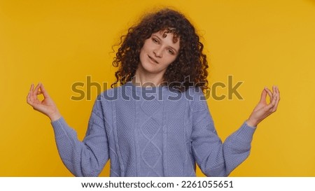 Keep calm down, relax, inner balance. Curly haired woman breathes deeply with mudra gesture, eyes closed, meditating with concentrated thoughts, peaceful mind. Young girl on yellow studio background
