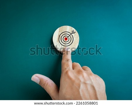 Business achievement goal and objective target concepts. Target icon on round wooden block pointing by businessman hand on blue background.