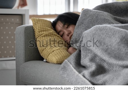 Sick Asian woman sleeping resting on sofa under blanket at home, recovering from flu. Sleepy weak female lying on couch suffering from fever and chills during sickness, having symptoms of Influenza Royalty-Free Stock Photo #2261075815
