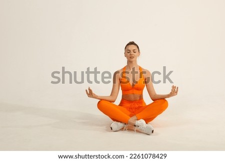 Young positive smiling woman doing yoga asana in orange fitness sport outfit cloth studio isolated shot. Royalty-Free Stock Photo #2261078429