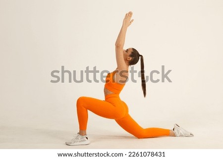 Young positive smiling woman doing yoga asana in orange fitness sport outfit cloth studio isolated shot. Royalty-Free Stock Photo #2261078431